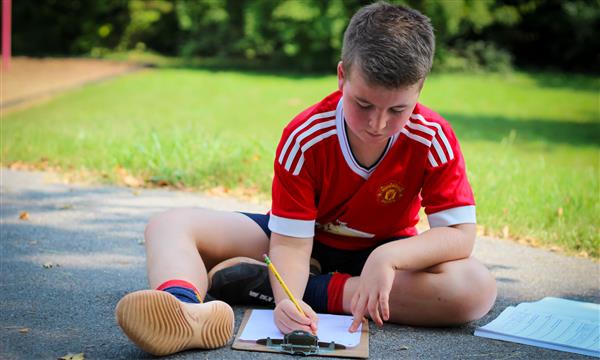 student writes on clipboard outside
